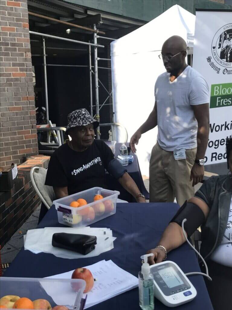 Volunteer checking blood pressure at an outdoor table, side view
