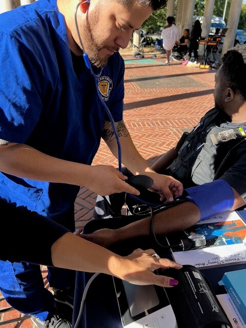 Volunteer checking a man's blood pressure outdoors, nurse in blue